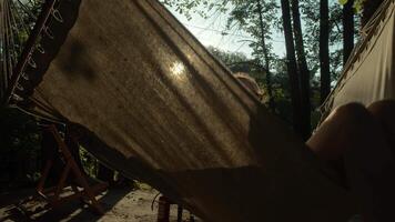 Silhouette of a girl, swinging in the summer breeze on a hammock, bathed in the warm rays of the setting sun. video