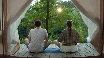 Couple sits down in a lotus position, surrounded by nature, and begins to meditate. View from their tent video