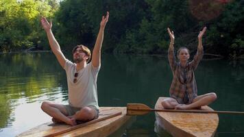 Young woman and a man are sitting on a surfboard in the lotus position, practicing breathing exercises. video
