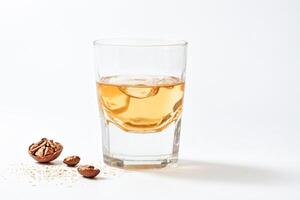 Glass of golden liquid with walnut shells on white background photo