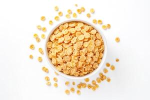 Bowl of corn flakes with scattered flakes around photo