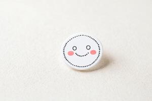 White Smiley Face Button with Black Outline and Pink Cheeks on a White Surface photo
