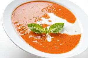Close-up of a bowl of tomato soup with a swirl of cream and basil leaves photo