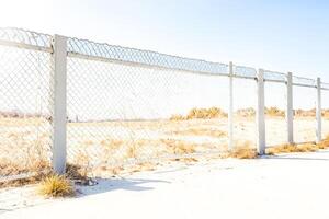 Chain Link Fence with White Posts in Front of Dry Grass Field photo