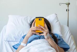 Patient woman lying on bed in hospital and receiving intravenous fluid directly into a vein but she still playing her social network on smartphone. photo