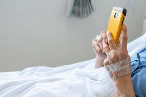 Cropped shot of patient hand receiving intravenous fluid directly into a vein but she still playing her social network on smartphone. photo