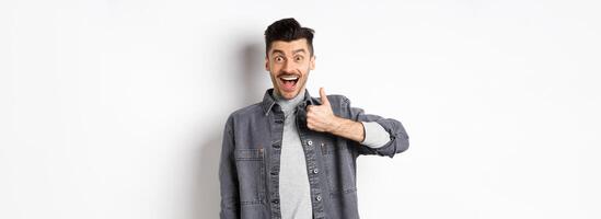 Well done, very good. Excited handsome guy praising nice work, showing thumb up and smiling happy, approve awesome choice, standing on white background photo