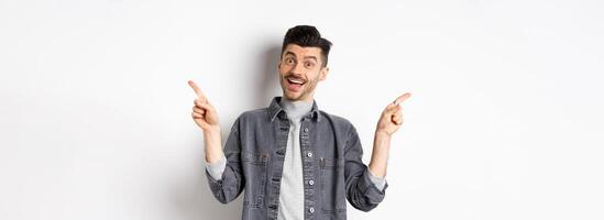 Cheerful smiling man pointing fingers sideways, showing left and right ways, looking happy at camera, standing on white background photo