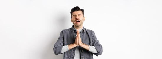 Miserable man begging for help, need something and crying, pleading with sad face, standing on white background desperate photo