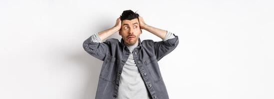 Guy looking aside in panic, stare at logo nervous and alarmed, having trouble, holding hands on head, standing on white background photo