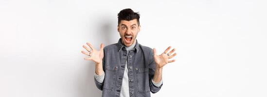Angry man scream and look scary at camera, shouting with furious and hateful expression, standing on white background photo