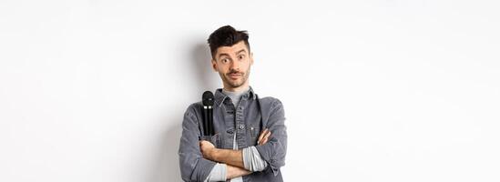 Image of funny male entertainer or singer, holding microphone in pocket of jacket and look at camera with arms crossed, standing against white background photo