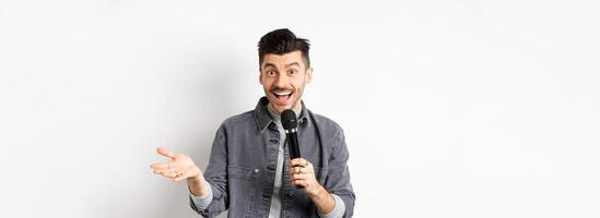 Handsome smiling performer talking in mic, gesturing and performing, making speech with microphone, standing against white background photo
