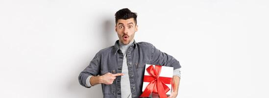 Happy Valentines day. Man shopping for romantic date, pointing at gift box and looking amazed, saying wow impressed, showing lover present, white background photo