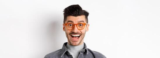 Excited handsome man in trendy eyewear checking out awesome promo, smiling amused, standing happy on white background photo