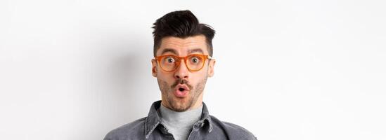 Wow look there. Excited handsome man in stylish glasses stare impressed at camera, checking out eyewear store offer, standing on white background photo