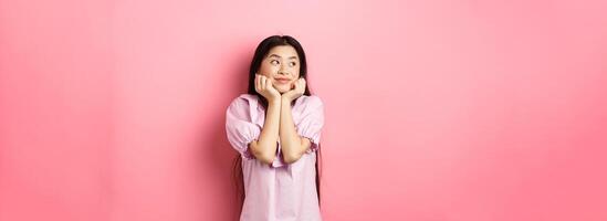 Dreamy romantic girl looking aside at logo and smiling, thinking of something beautiful, standing on pink background photo