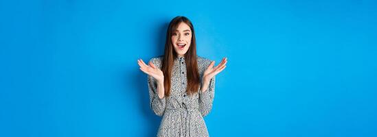 Excited beautiful woman clap hands and congratulate you, praising nice work, applause at camera and smiling, standing on blue background photo