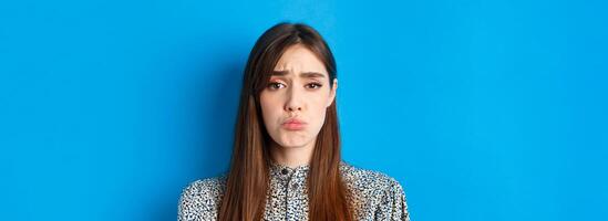 People emotions concept. Sad cute girl begging for something, pucker lips and frowning, whining asking please, standing on blue background photo