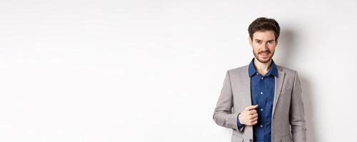 Confident businessman in suit smiling at camera, standing self-assured against white background photo