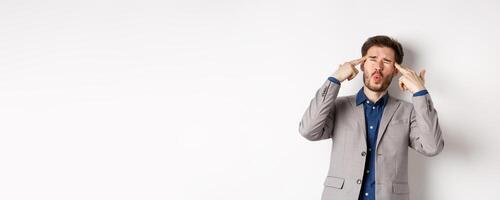 Distressed and tensed businessman pointing at head and complaining, feeling annoyed with situation blowing his mind, standing bothered on white background photo