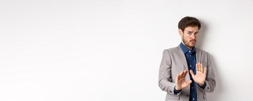 Stay away. Reluctant businessman step back with concerned disgusted face, raising hands to block bad offer, rejecting something awful, telling no and decline proposal, white background photo