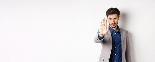 Hold right there. Serious businessman in suit stretch out hand and tell to stop, frowning and look confident, disapprove action, prohibit something bad, standing on white background photo