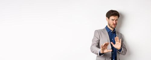 Stay away. Reluctant businessman step back with concerned disgusted face, raising hands to block bad offer, rejecting something awful, telling no and decline proposal, white background photo