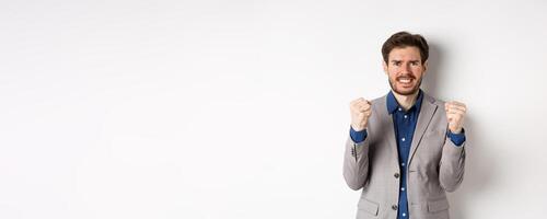 Tensed businessman feeling nervous and pressured, clenching fists and teeth, staring at camera, making money and looking worried, standing on white background photo