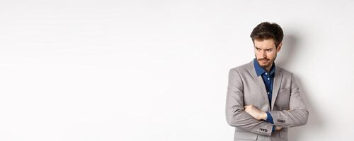 Moody guy in suit looking aside with unfair face, cross arms on chest and frowning angry, standing upset against white background photo