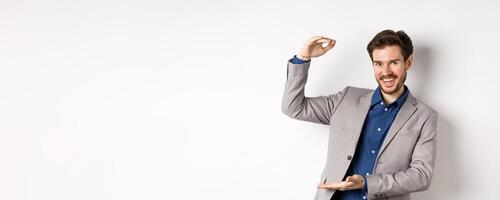 Successful businessman showing big size, shape large object and smiling pleased, standing on white background in suit photo