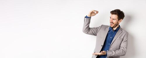 Smiling happy businessman in suit showing large size object, shaping big thing with hands and look pleased, standing on white background photo