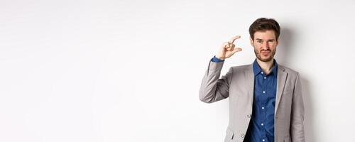 Disappointed businessman showing small size and grimacing upset, little income, standing displeased against white background photo