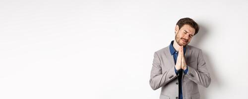 Pleading businessman begging for help, holding hands in pray and asking for favour, need something, say please, standing on white background photo