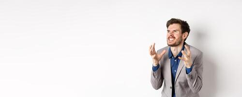 Angry man in business suit look left with hatred, stare aside and shaking hands with clenched teeth, standing mad and furious, wanting to kill someone, white background photo