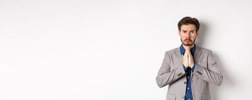Miserable whining businessman asking for loan, need help and begging you, sobbing and say please with sad face, standing on white background, ask for forgiveness photo