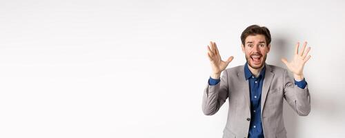 Businessman scream and shake hands in panic, look alarmed and anxious, shouting at camera, standing in suit on white background photo