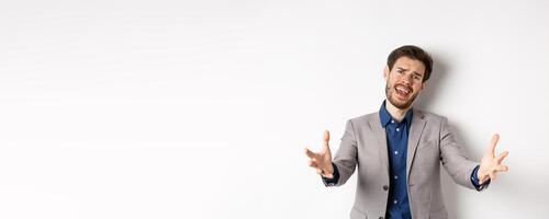 Desperate businessman stretch out hands and frowning disappointed, losing in game and feeling unfair, standing in suit on white background photo