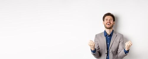Excited man winning in cazino and celebrating, making fist pump and shouting yes with happy expression, achieve goal, triumphing, standing on white background photo