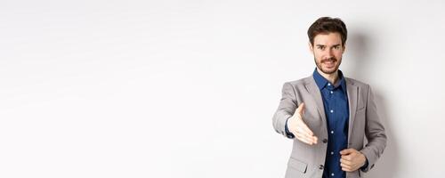 Confident businessman stretch out hand for business handshake and smiling, introduce himself on meeting, standing on white background photo
