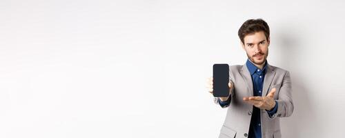 E-commerce and online shopping concept. Man demonstrated empty smartphone screen to you, showing phone display to introduce something, standing on white background photo
