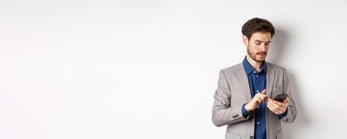 Handsome businessman in stylish suit chatting on smartphone, using mobile phone, standing on white background photo