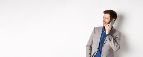 Happy businessman laughing and smiling, talking on mobile phone, holding hand in pocket and looking aside at empty space with cheerful face, white background photo