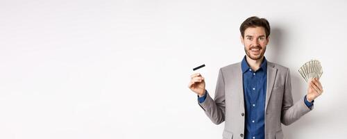 Happy successful businessman in suit showing money and credit card, smiling at camera, white background photo