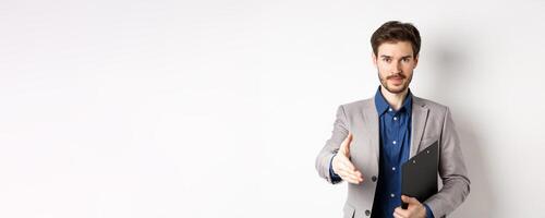 Confident businessman with clipboard giving hand for handshake, greeting business partners on meeting, standing on white background in suit photo