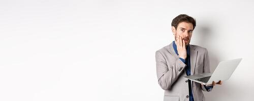 Shocked and troubled businessman have trouble on laptop, looking worried at camera, made mistake at work, standing on white background in suit photo