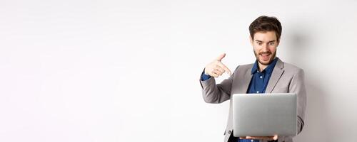 Excited male ceo manager looking and pointing at laptop with amazed smile, checking out special deal online, standing on white background photo