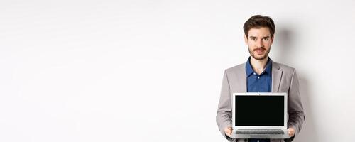 Handsome caucasian businessman in suit showing empty laptop screen, demonstrate promo, standing on white background photo