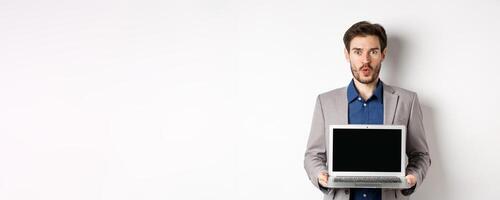 Handsome caucasian businessman in suit showing empty laptop screen, demonstrate promo, standing on white background photo