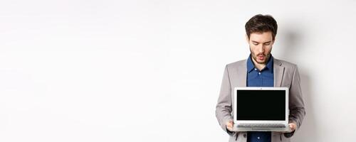 Handsome caucasian businessman in suit showing empty laptop screen, demonstrate promo, standing on white background photo